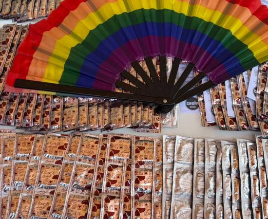 Una mesa con preservativos y un abanico de los colores de la diversidad sexual.