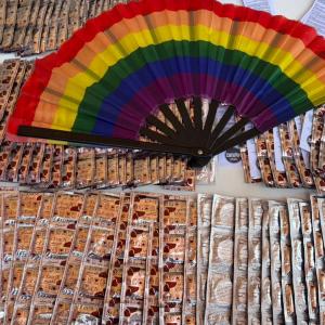 Una mesa con preservativos y un abanico de los colores de la diversidad sexual.